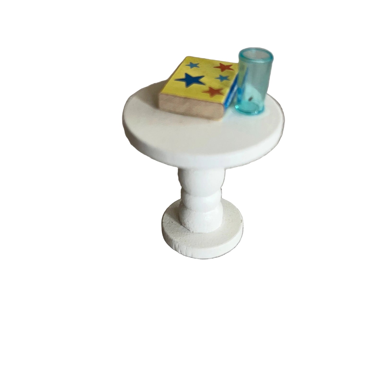 Small white dolls house table with a book and glass on a textured surface